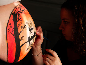 Woman painting on pregnant friend belly