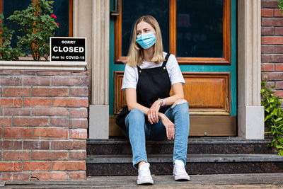 Full length portrait of young woman standing against brick wall