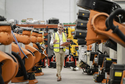 Engineer holding file folder and eyeglasses walking in factory