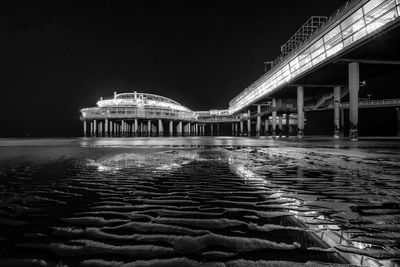 Illuminated scheveningen pier in sea against sky at night