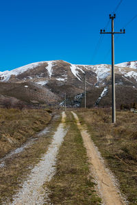 Road amidst snowcapped mountains against clear blue sky