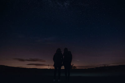 Silhouette friends walking on field against sky at night