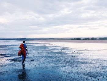 Woman walking on snow covered beach against sky