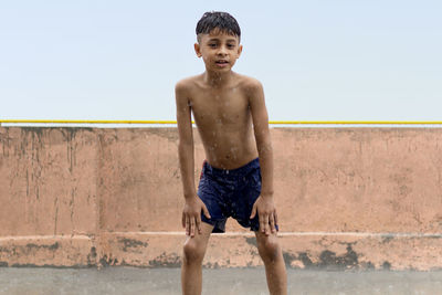 One skinny wet boy playing and having fun in rain at his terrace, outdoors during monsoon season.