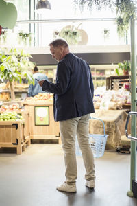 Rear view of mature man using smart phone in supermarket