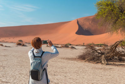 Rear view of woman photographing desert through mobile phone