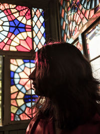 Young woman looking away while sitting against glass window