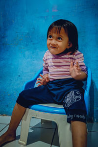 Portrait of cute girl sitting against blue wall