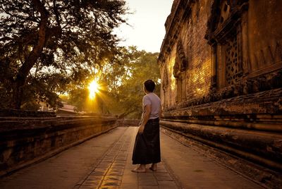 Rear view of woman walking on walkway at sunset