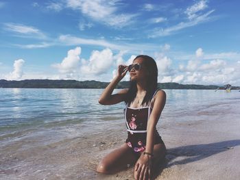 Full length of woman sitting on beach against sky