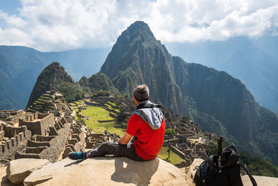 Rear view of man sitting on mountain against machu picchu