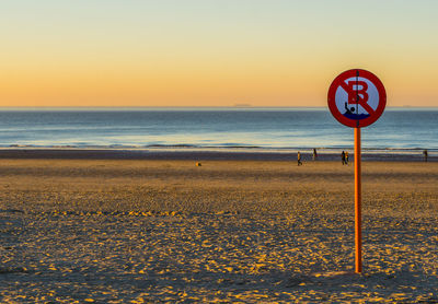 Information sign on beach against sky during sunset