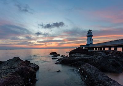 Lighthouse by sea against sky during sunset