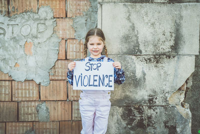 Portrait of girl holding poster against wall