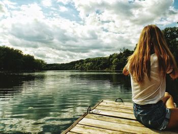 Rear view of woman sitting on floating platform in lake against sky