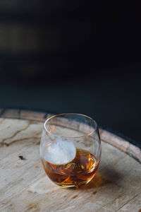 Close-up of whiskey in glass with ice sphere on bourbon barrel 