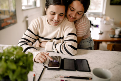 Woman using smart phone on table while embraced by daughter at home