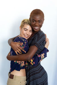 Portrait of smiling lesbian couple embracing against white background