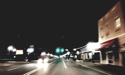 Cars on illuminated road against clear sky at night