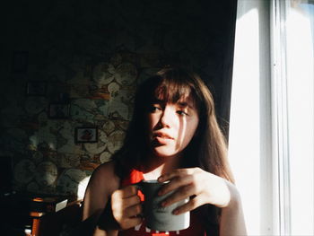 Thoughtful young woman holding coffee cup by window at home