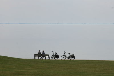 People riding bicycle by lake against sky