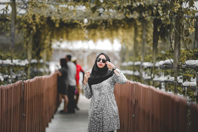 Portrait of woman standing on railing against trees