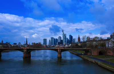 Bridge over river by buildings against sky in city