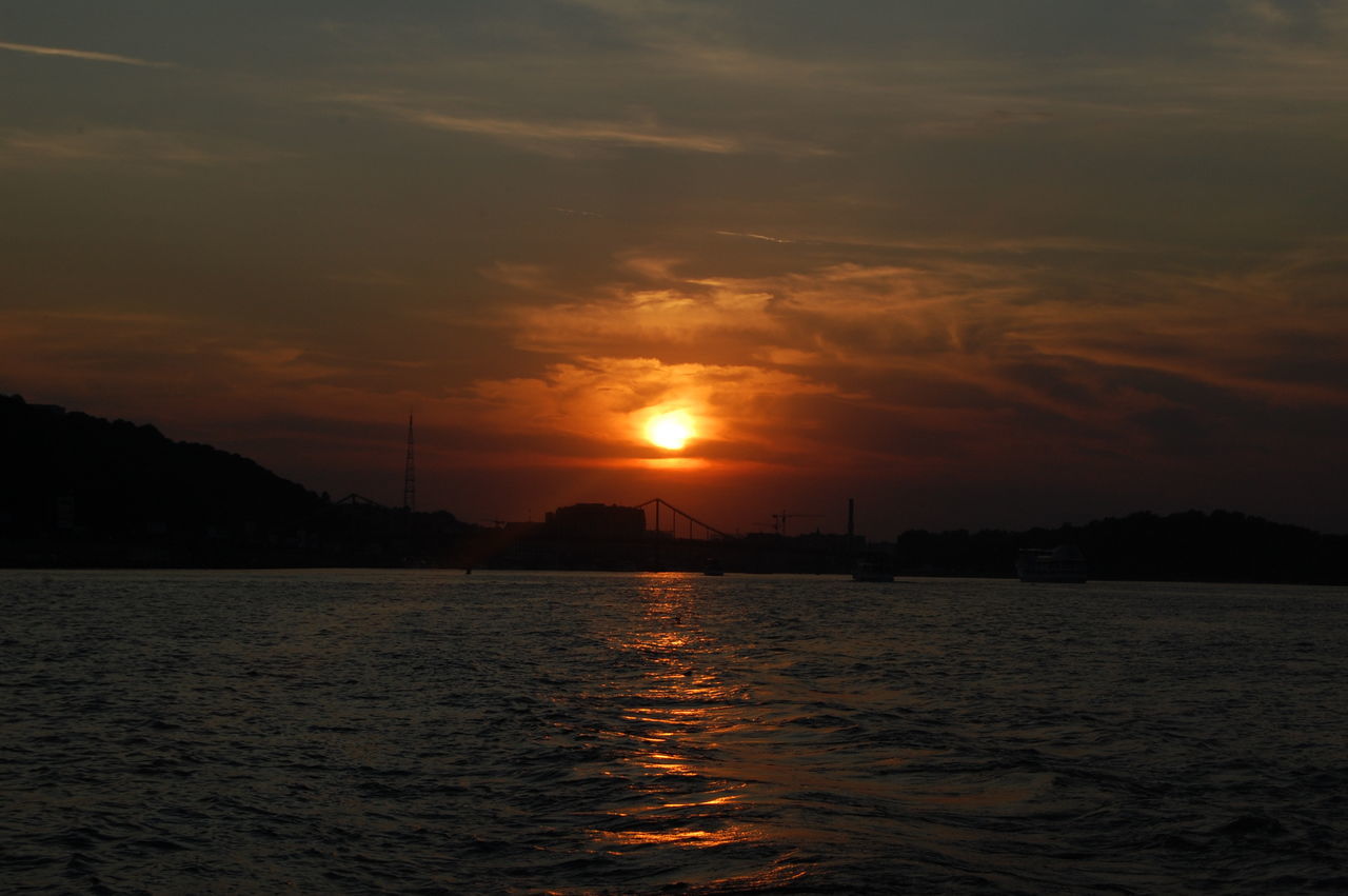 sunset, water, waterfront, sky, sun, silhouette, scenics, orange color, beauty in nature, tranquil scene, rippled, tranquility, cloud - sky, nature, river, idyllic, sea, mountain, built structure, sunlight