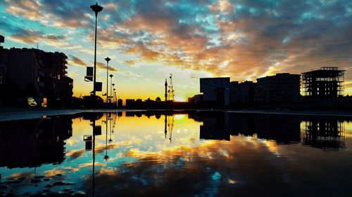 Silhouette buildings by lake against sky during sunset