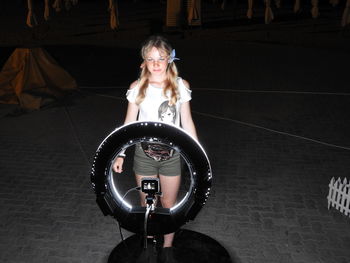 Smiling girl standing against illuminated camera at night