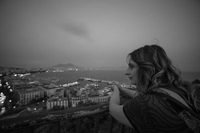 Side view of young woman looking at cityscape against sky