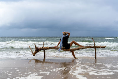 Rear view of woman standing at beach against sky