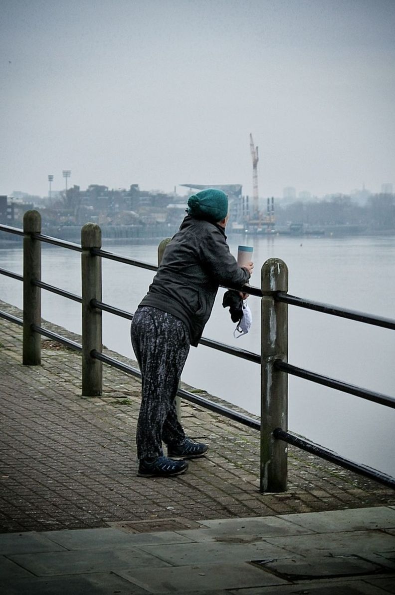 water, one person, sky, full length, railing, sea, nature, blue, adult, men, ocean, pier, lifestyles, side view, leisure activity, architecture, beauty in nature, day, scenics - nature, winter, outdoors, clothing, black, casual clothing, morning, fog, white, activity, tranquil scene, hood, standing, tranquility, city, reflection