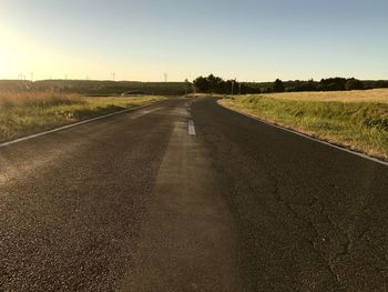 Country road amidst field against sky
