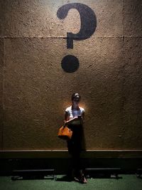 Woman using phone while standing below question mark on wall at night