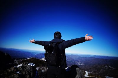 Man standing on rock against blue sky