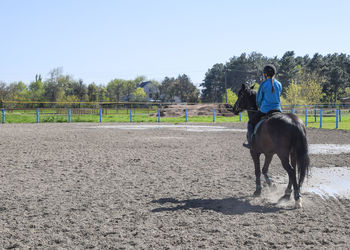 Rear view of girl riding horse at ranch