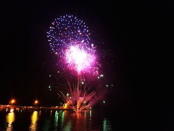 Low angle view of firework display over river against sky at night