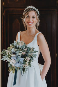 Portrait of bride holding bouquet standing against wall
