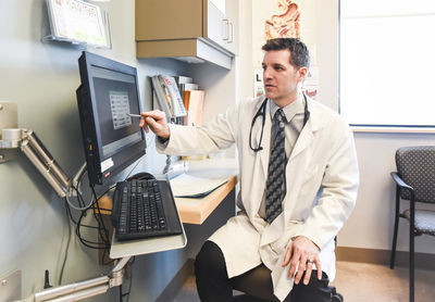 Doctor in white coat pointing at computer screen in a clinic room.