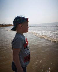 Boy looking away in sea against sky