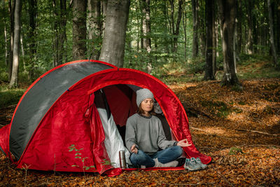 Tranquil female traveler sitting in lotus pose near camping tent and meditating with closed eyes in woods