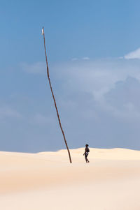 Man on sand dune in desert in front of a high rod against sky