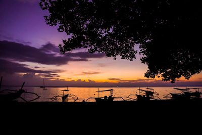 Silhouette of tree by sea against dramatic sky