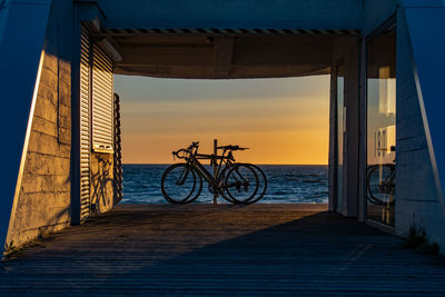 Bicycle by sea against sky during sunset