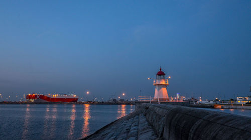 Lighthouse by sea against blue sky