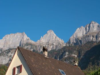 Low angle view of houses and mountains against clear blue sky