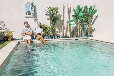 Brother and sister relaxing by swimming pool on sunny day