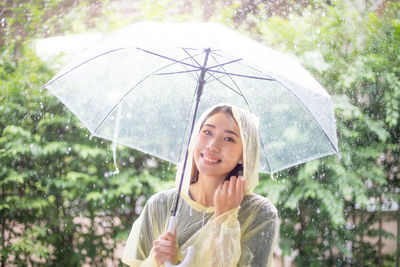 Smiling woman holding wet umbrella during rainy season