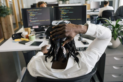 Rear view of male computer programmer sitting with head in hand at office